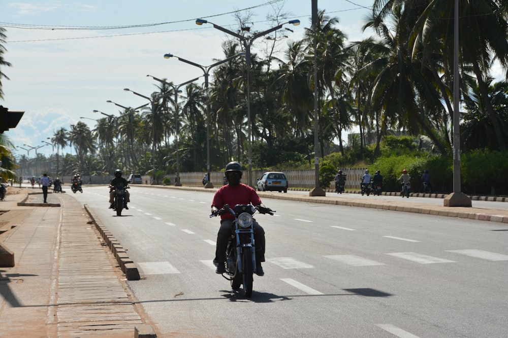 a man riding a motorcycle down a street next to palm trees