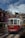 A classic red and white tram is moving down a cobblestone street lined with picturesque buildings. The tram is part of a city tour service, as indicated by the 'HILLS TRAMCAR TOUR' sign. The sky is partly cloudy, and there are a few people walking by on the street.