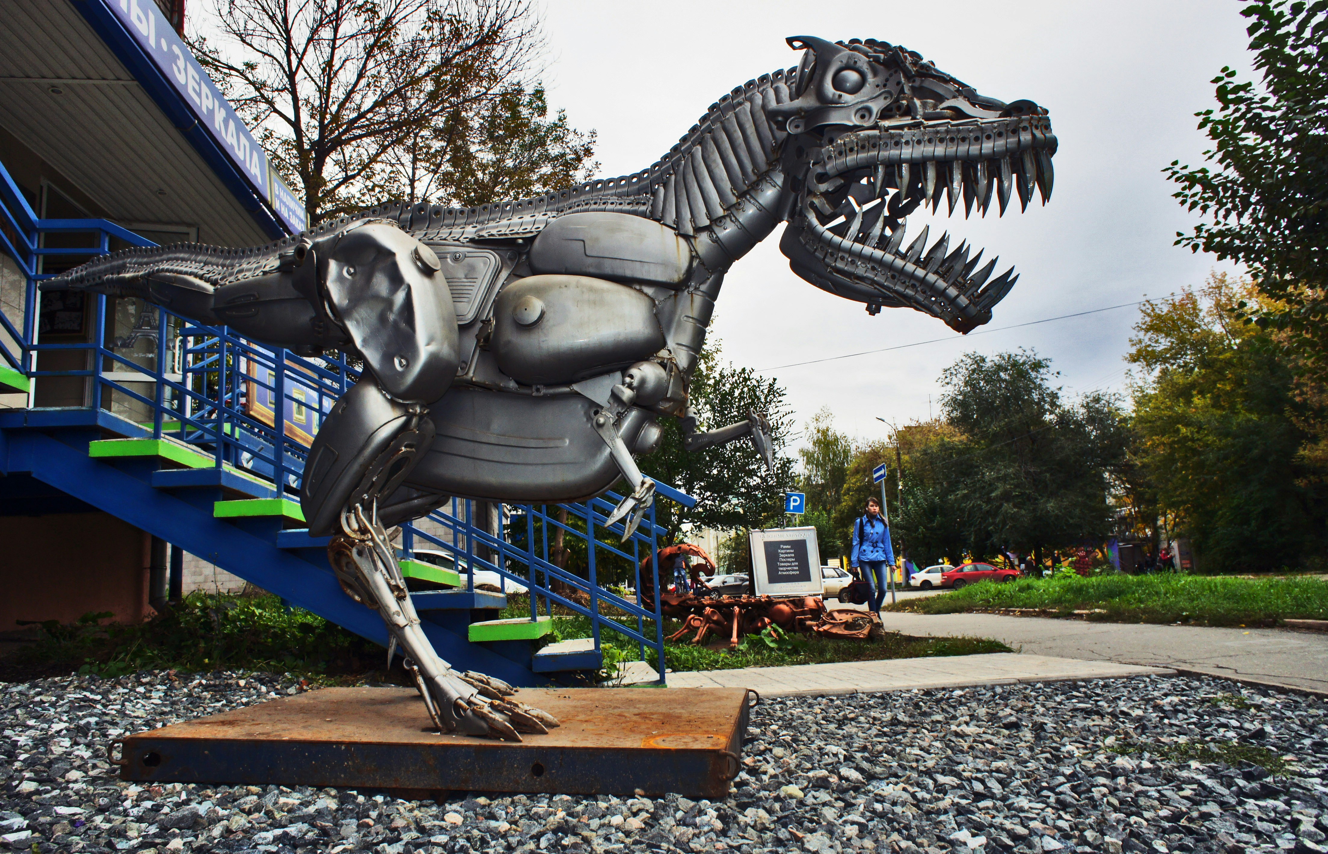 a metal dinosaur statue in front of a building