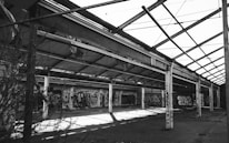 A large, abandoned industrial warehouse with a partially collapsed roof structure. Walls are covered with colorful graffiti, showcasing various artistic styles. The scene is devoid of people, and vegetation is encroaching through the open spaces.