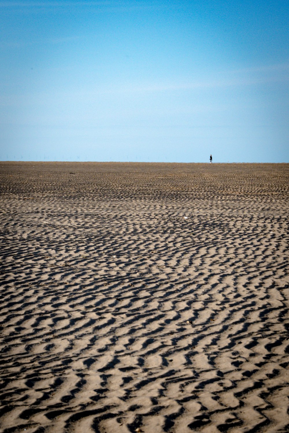a person walking across a sandy beach under a blue sky