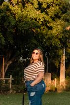 A confident woman in her 40s smiling outdoors surrounded by greenery.