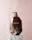 A brown bottle of Moroccan Argan Oil conditioner is positioned on a white pedestal against a soft pink background. Water splashes around the bottle, giving a dynamic and refreshing feel.