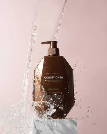 Close-up of a luxurious argan oil bottle surrounded by hibiscus flowers on a cream beige background.