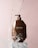 A brown bottle of Moroccan Argan Oil conditioner is positioned on a white pedestal against a soft pink background. Water splashes around the bottle, giving a dynamic and refreshing feel.