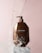 A brown bottle of Moroccan Argan Oil conditioner is positioned on a white pedestal against a soft pink background. Water splashes around the bottle, giving a dynamic and refreshing feel.