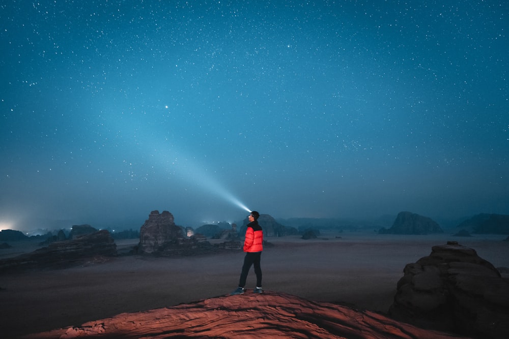 une personne debout au sommet d’un rocher sous un ciel rempli d’étoiles