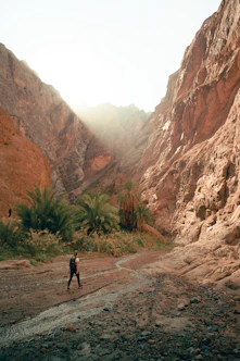 a man walking down a dirt road next to a mountain