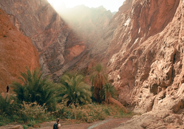 a man walking down a dirt road next to a mountain