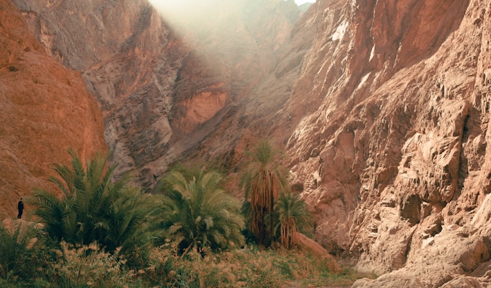 a man walking down a dirt road next to a mountain