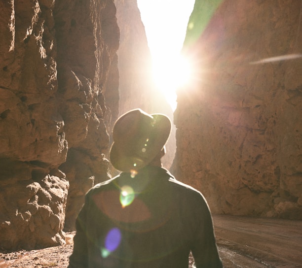 a man standing in a canyon with the sun shining through the rocks