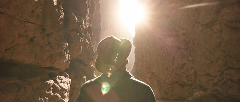 a man standing in a canyon with the sun shining through the rocks