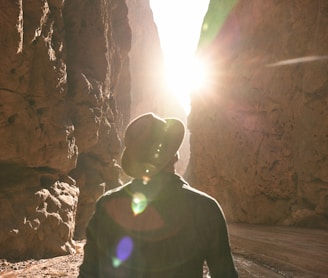 a man standing in a canyon with the sun shining through the rocks