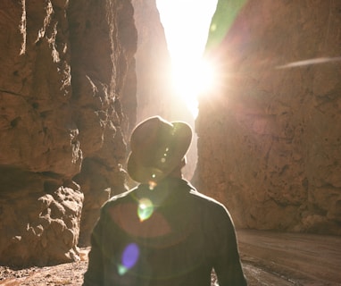 a man standing in a canyon with the sun shining through the rocks