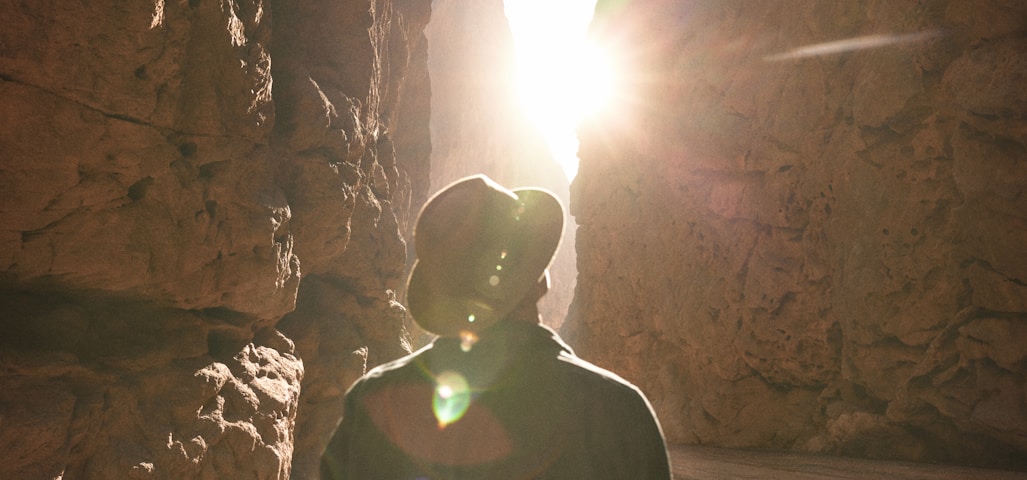 a man standing in a canyon with the sun shining through the rocks