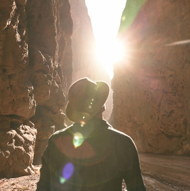 a man standing in a canyon with the sun shining through the rocks