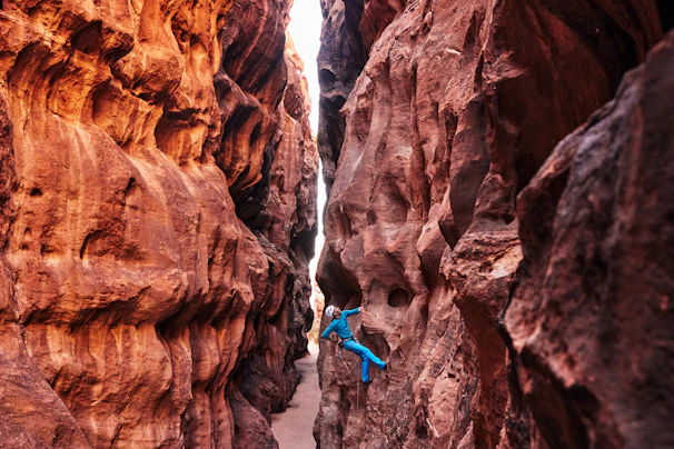 A canyoneer rappelling down a narrow slot canyon with textured red rock walls glowing in sunlight.
