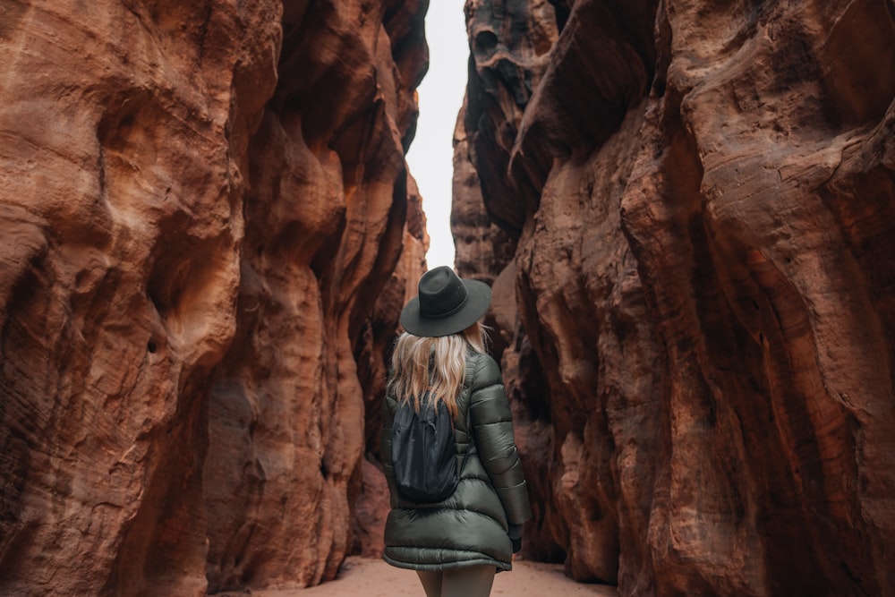 a woman in a hat and coat walking through a canyon