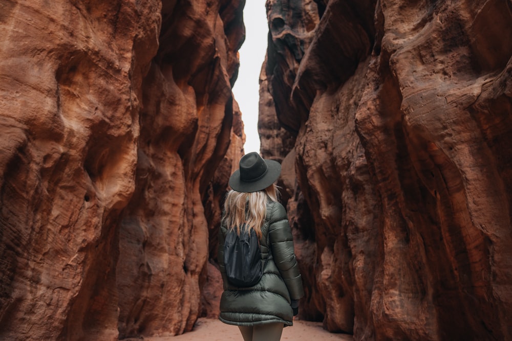 Une femme en chapeau et manteau marchant dans un canyon
