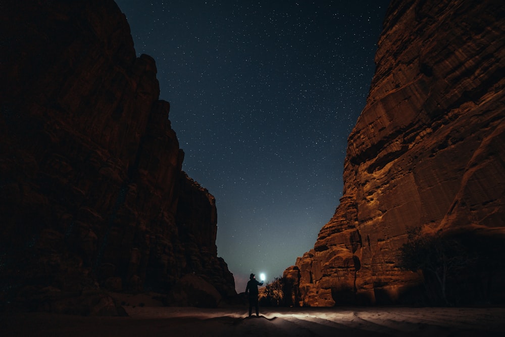 Una persona parada en medio de un cañón por la noche