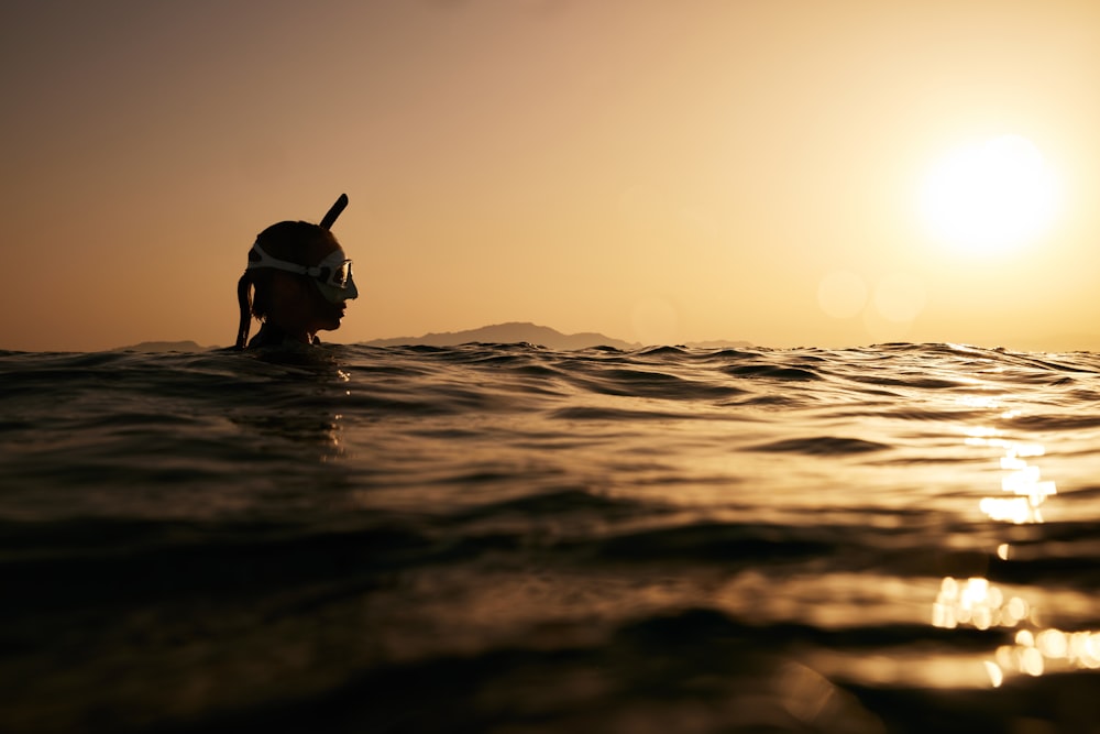 a person swimming in the ocean at sunset