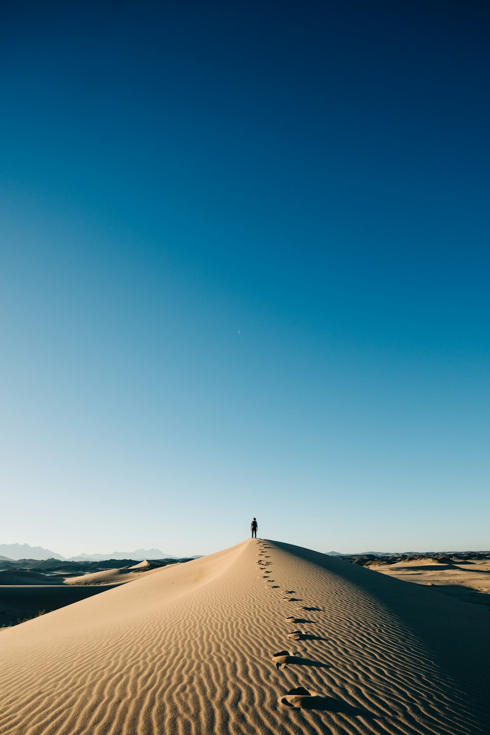 une personne debout au sommet d’une dune de sable