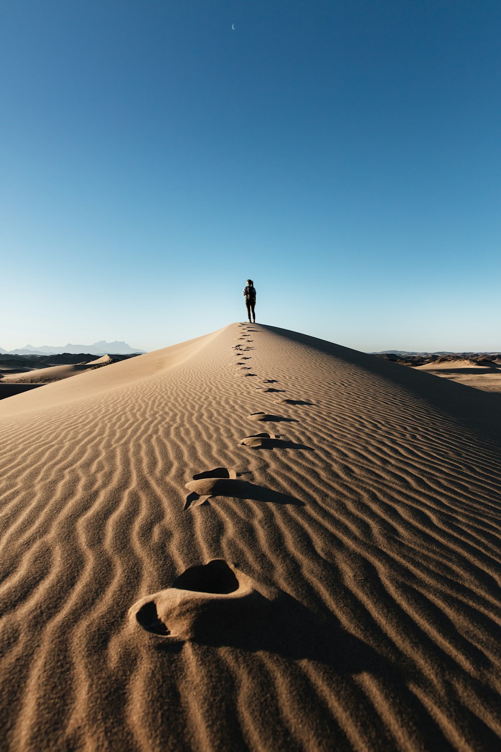 une personne debout au sommet d’une dune de sable