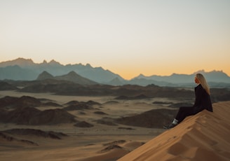 a woman sitting on top of a sand dune