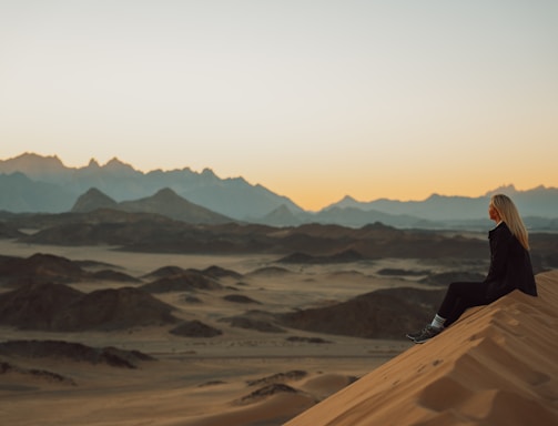 a woman sitting on top of a sand dune