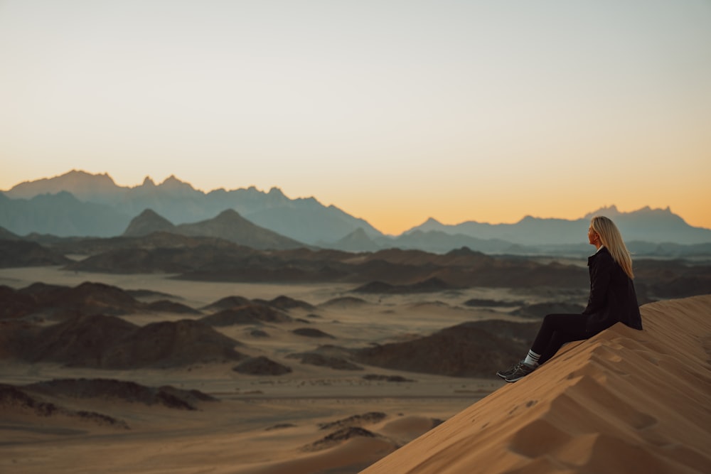 a woman sitting on top of a sand dune