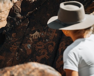 a man wearing a hat standing next to a rock