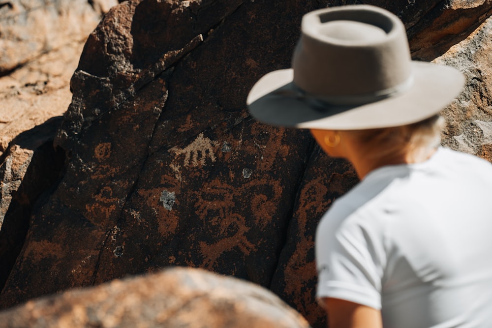 a man wearing a hat standing next to a rock