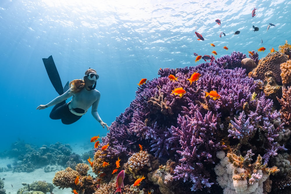 a woman scubas over a colorful coral reef