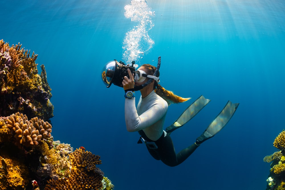 a woman scubas in the ocean with a camera