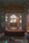 An ornate room featuring detailed, intricate wall designs with colorful stained glass windows. In the center, a low bed draped with a dark red cloth is positioned under a striped canopy. The walls are richly decorated with artistic patterns and depictions.