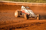 A close-up action shot of a dirt kart kicking up dust as it speeds around a corner at 221 Speedway.