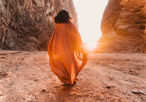 a woman in an orange dress walking through a canyon