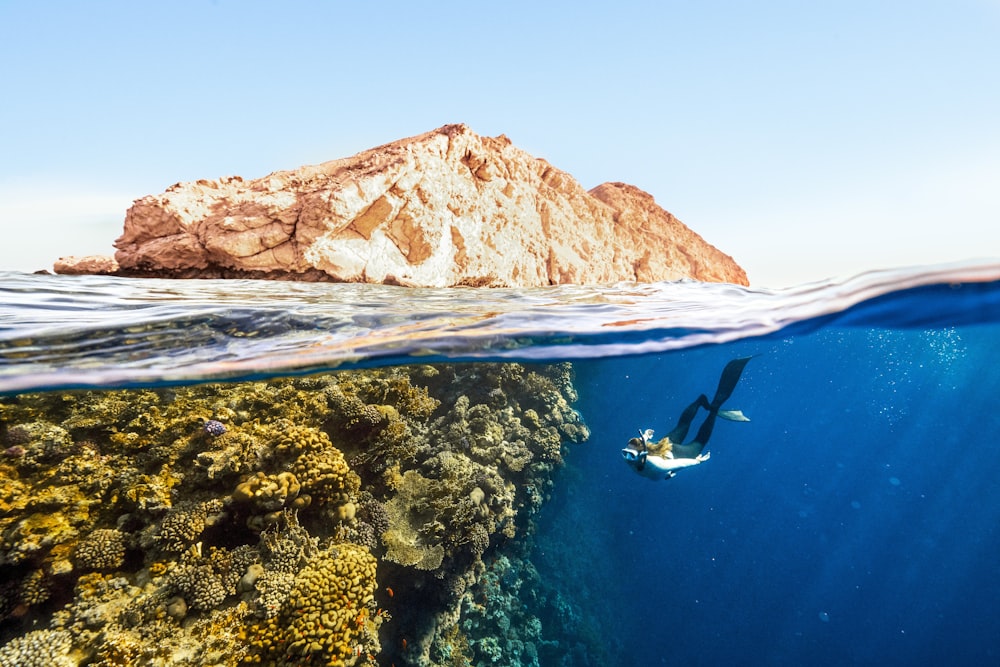 a person swimming in the ocean next to a rock