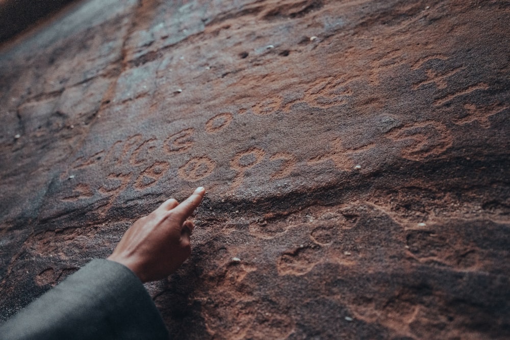 a person pointing at a rock with writing on it