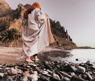 a woman standing on a rocky beach next to the ocean