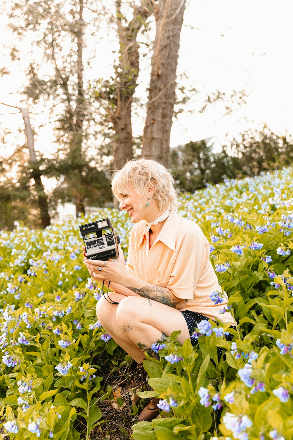 a woman sitting in a field of flowers holding a camera