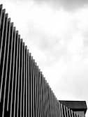 A modern architectural facade featuring vertically aligned slats that create a rhythmic pattern against a cloudy sky.