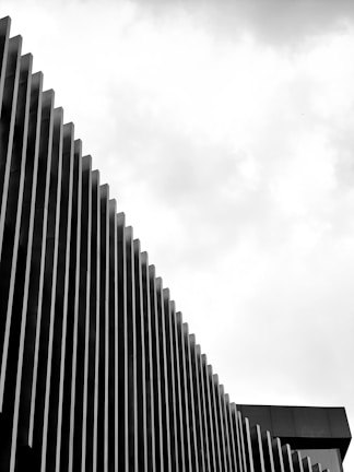 A modern architectural facade featuring vertically aligned slats that create a rhythmic pattern against a cloudy sky.