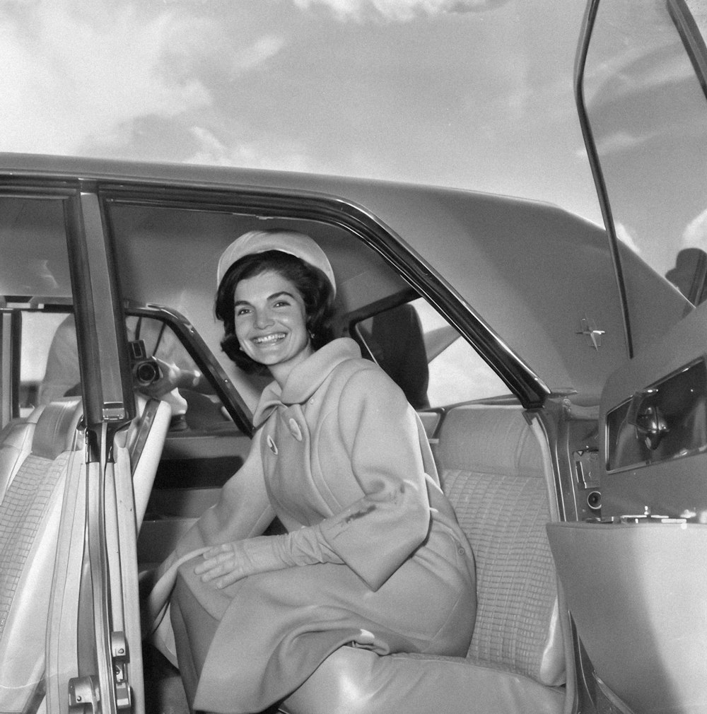 a black and white photo of a woman sitting in a car