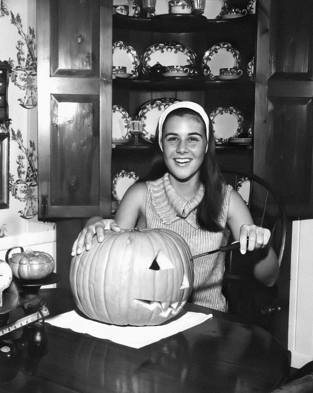 a black and white photo of a woman carving a pumpkin