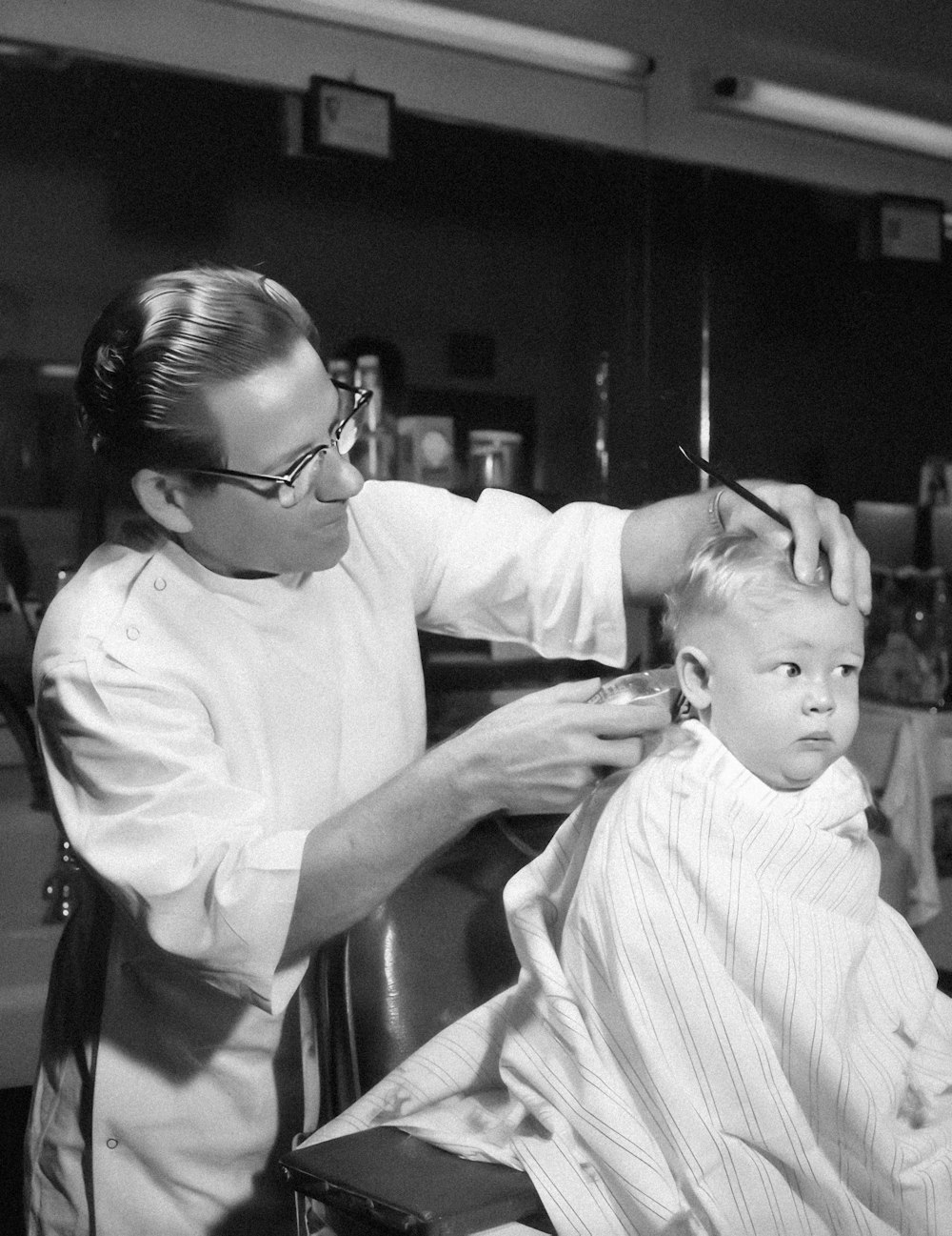 a black and white photo of a man cutting a young boy's hair