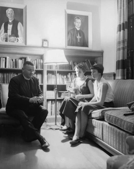 Portrait of Father Anderson Alves in a study filled with books and religious artifacts.