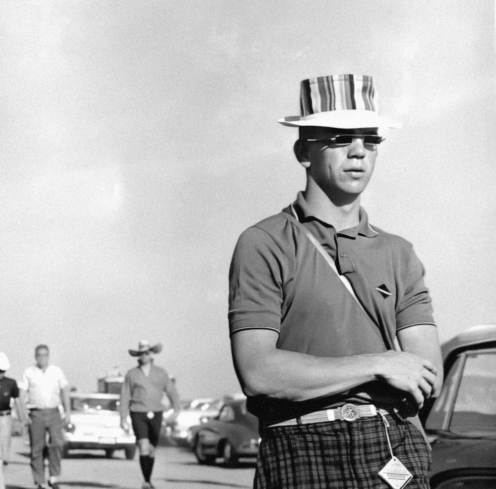a man in plaid shorts and a hat standing next to a car