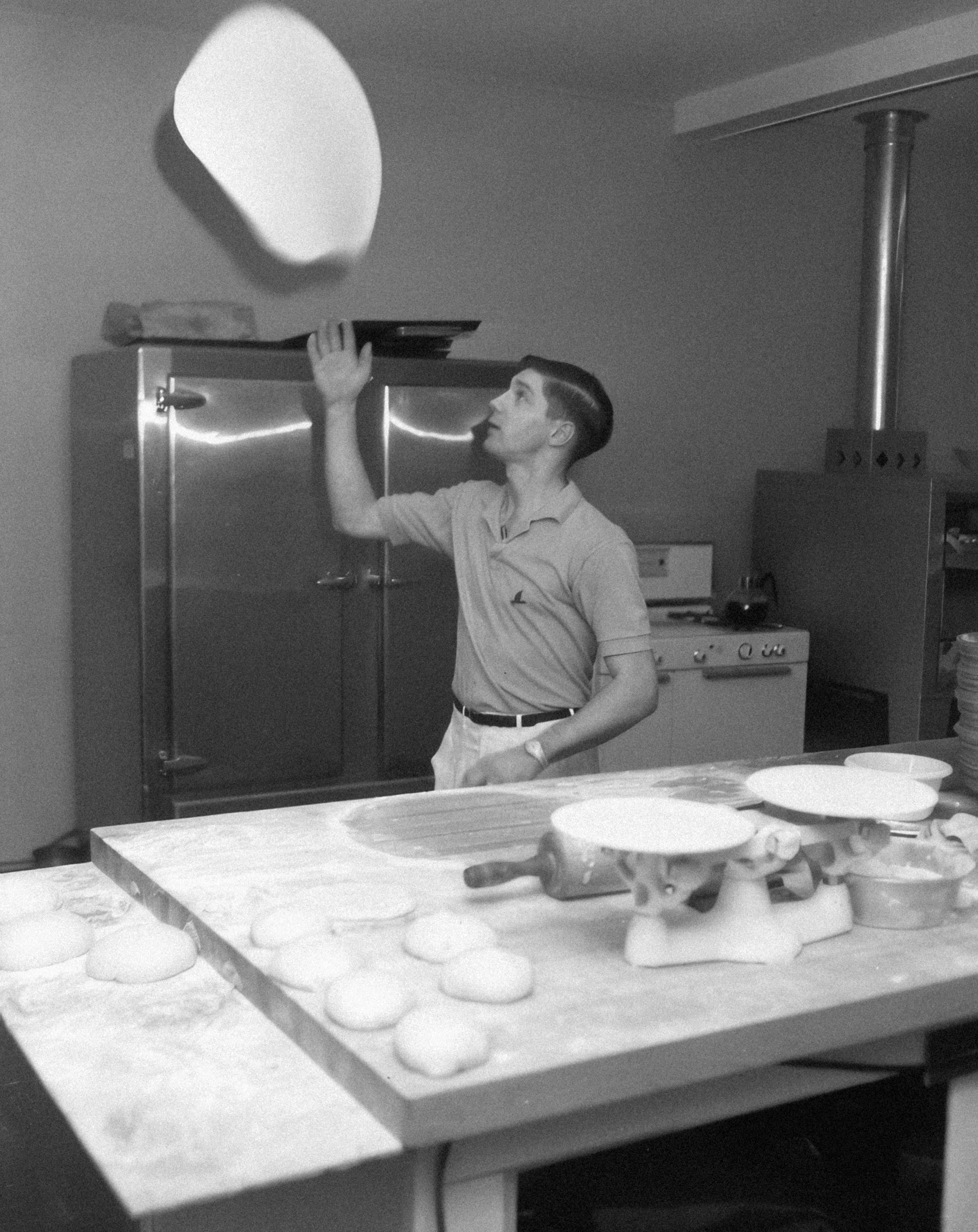 Un chef lanza masa de pizza al aire en una cocina.