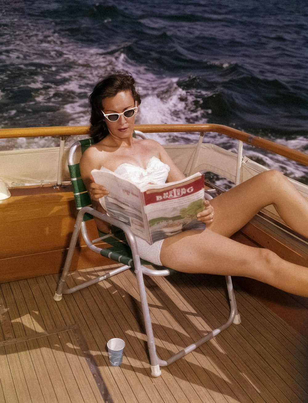 a woman sitting in a chair on a boat reading a magazine